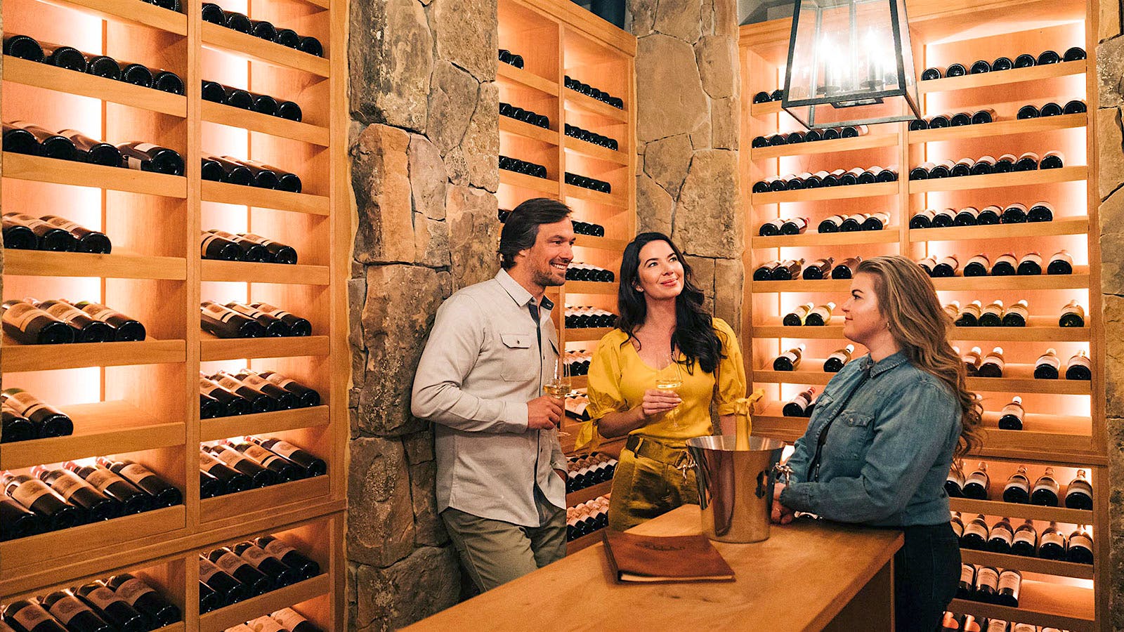 Three guests enjoying glasses of wine at a tasting table among The Cheyenne Club's display wine cellar