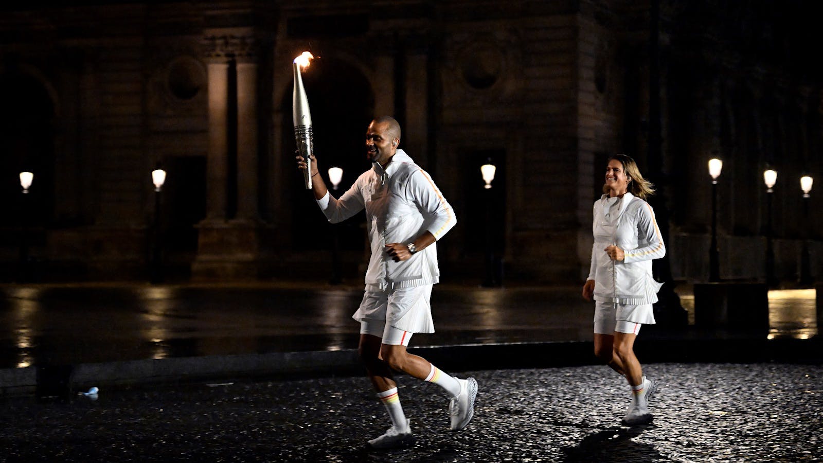 French athlete, NBA star and vintner Tony Parker takes the 2024 Olympic torch from tennis star Amélie Mauresmo