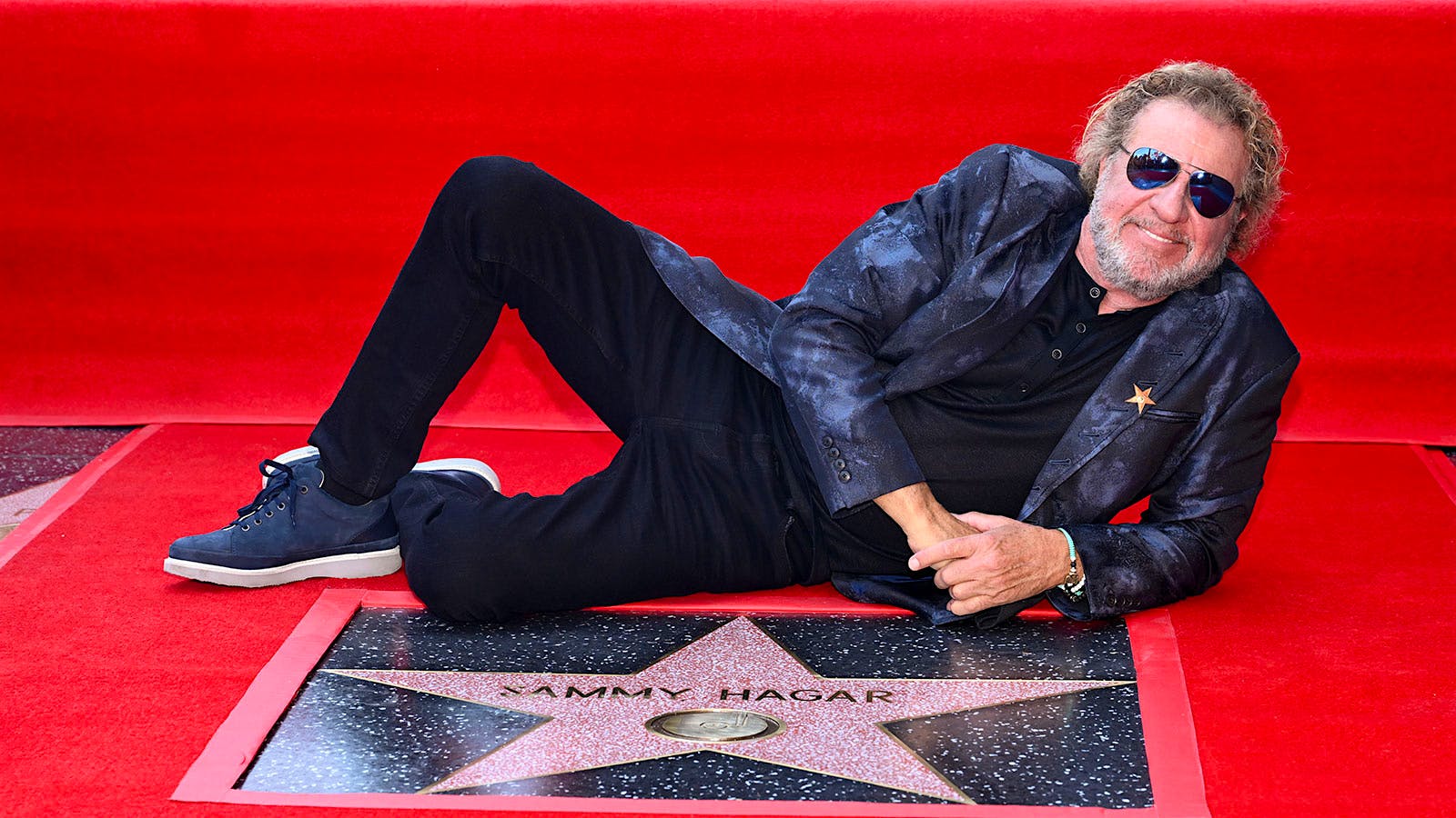 Sammy Hagar reclining on a red carpet next to his star on the Hollywood Walk of Fame