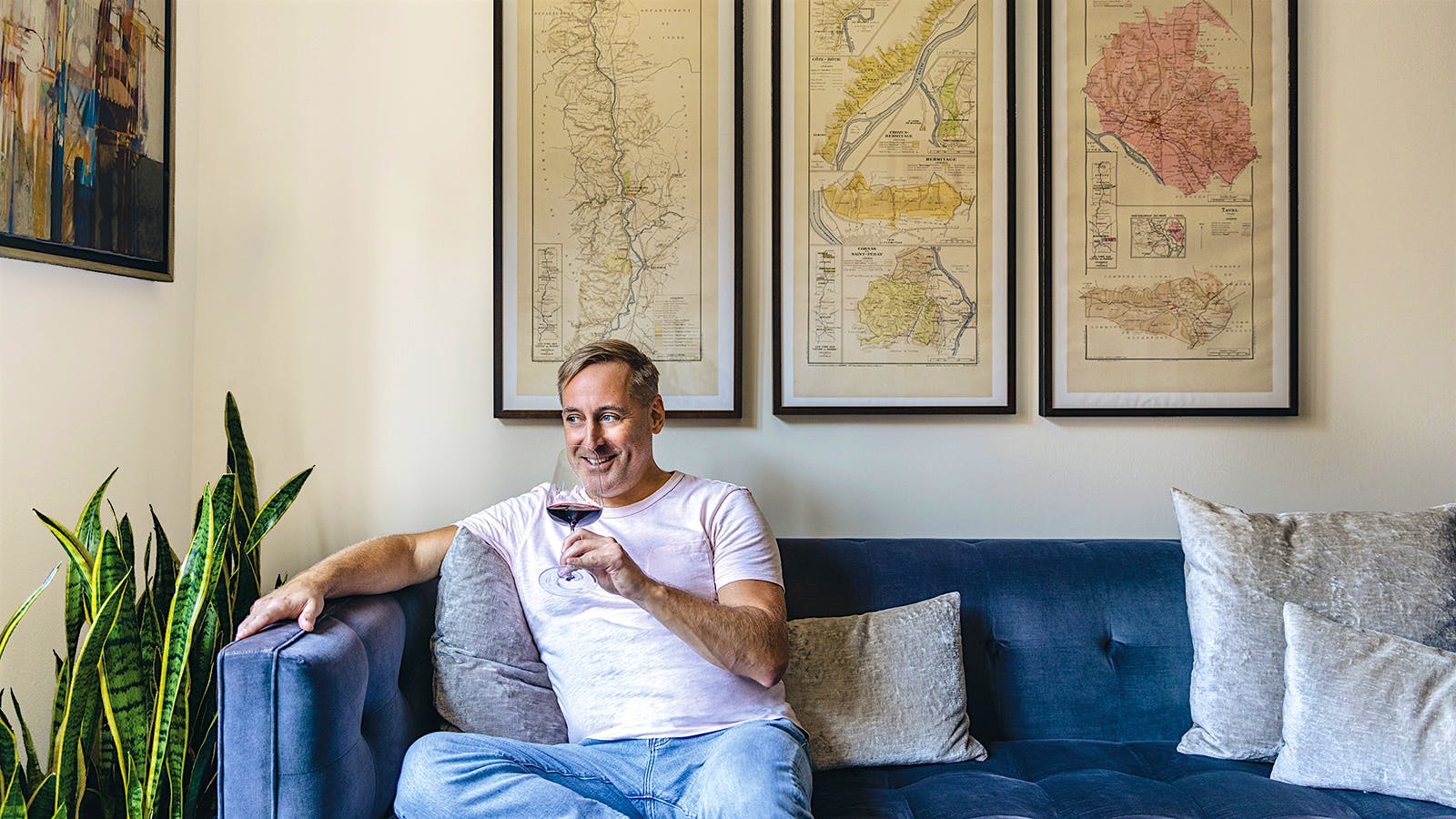 James Molesworth sipping a glass of wine on a couch in front of three wine region maps